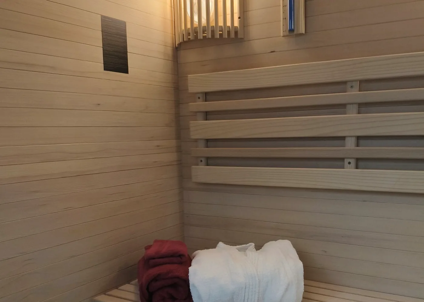 Sauna finlandeză: bancă de lemn cu prosoape bordo și albe.